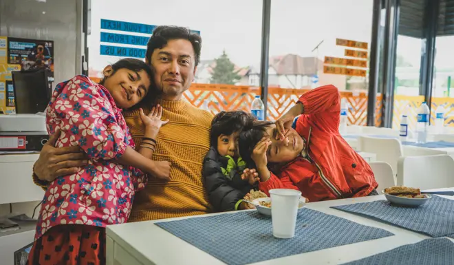 Denis and his children sit at a table in the Open Kitchen together. 