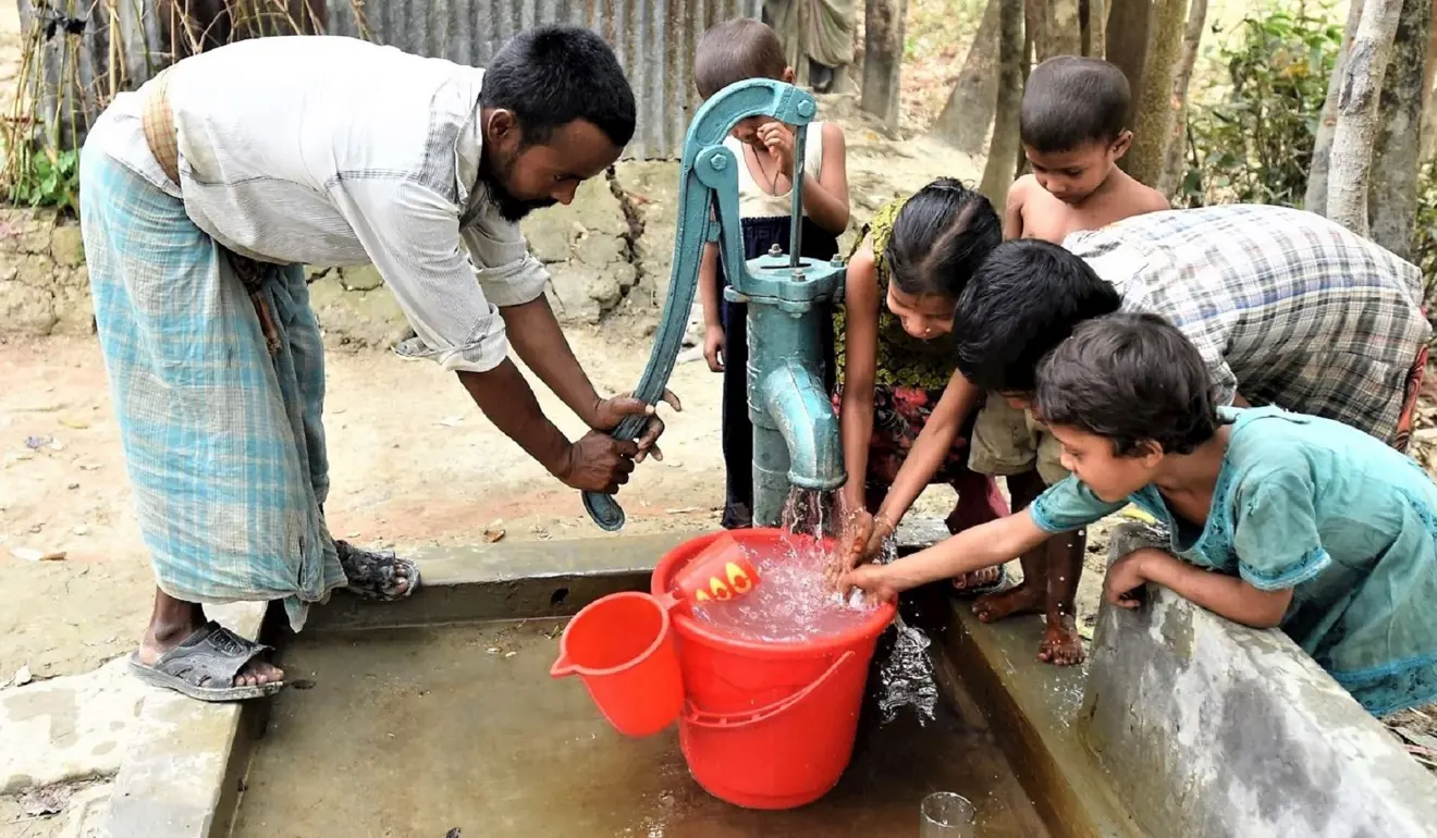 Man and children around a water well getting water