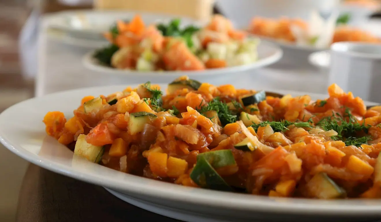 Plated dish of cooked onions, cucumber and tomato, garnished with dill