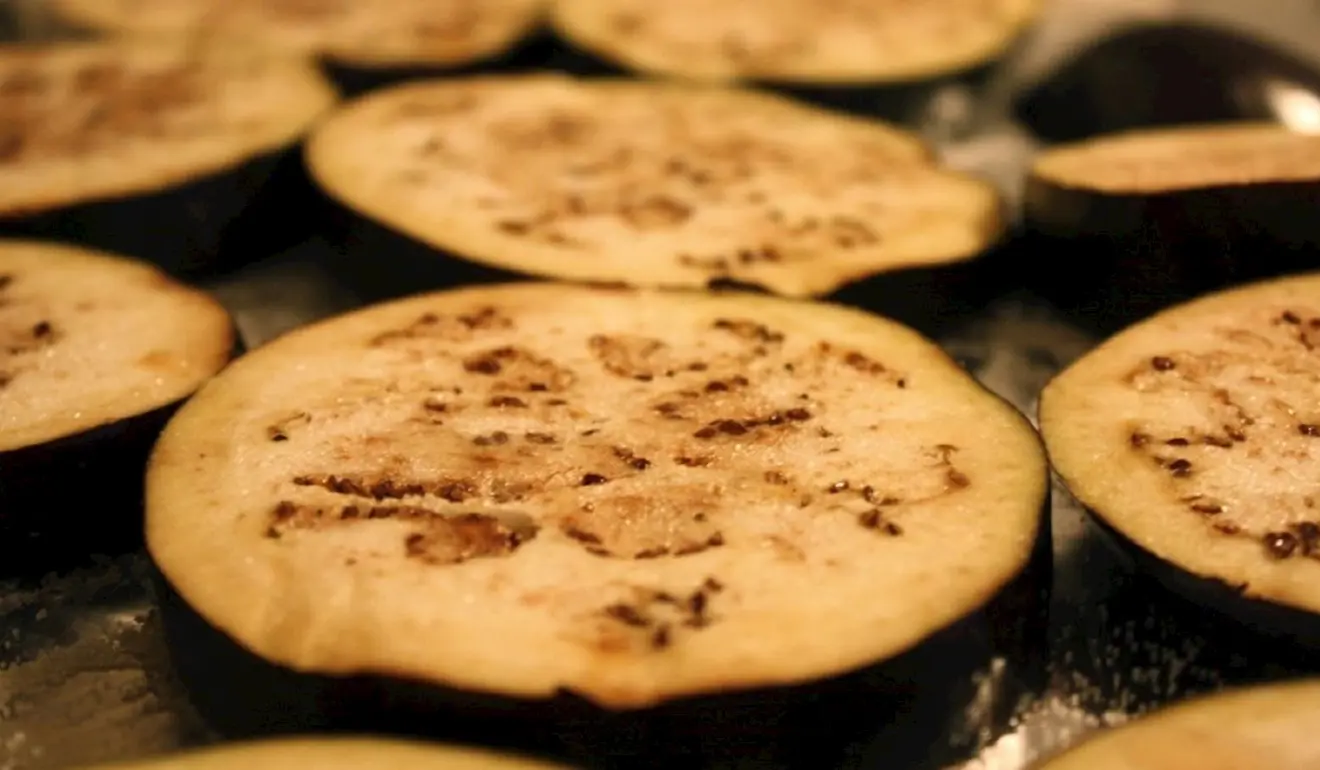 Cut-up slices of aubergine, sizzling on the stove, lightly seared and golden on one side.
