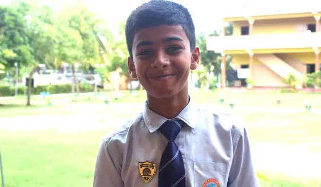 Jameer, an orphan in Sri Lanka smiles at the camera outside his school building. 