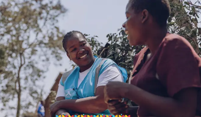 Muslim Hands volunteer in a high vis jacket is holding a collection bucket as a child drops in some coins. 