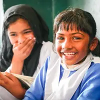 Two schoolgirls smile in front of a chalk board in a classroom