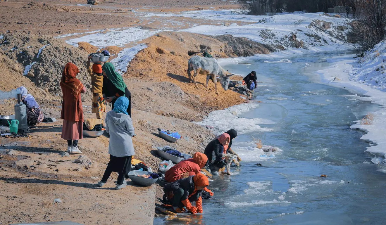 People washing their belongings in an icy river with barely enough layers on to keep them warm.