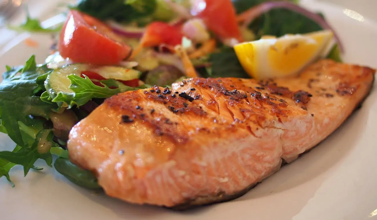 A dish of lightly seared salmon, served with a side of rocket and vegetables - and a wedge of lemon!